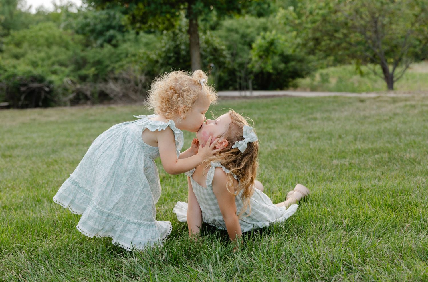 Two little girls in light blue dresses on green grass.