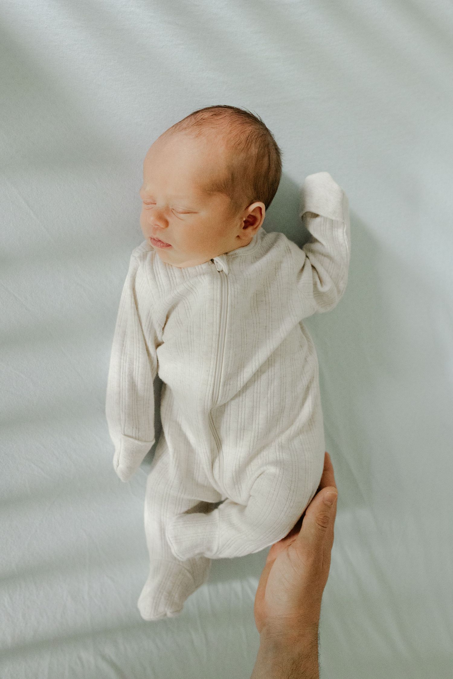 Sleeping newborn baby in cream ribbed zip-up footie pajamas lying on soft mint green blanket.