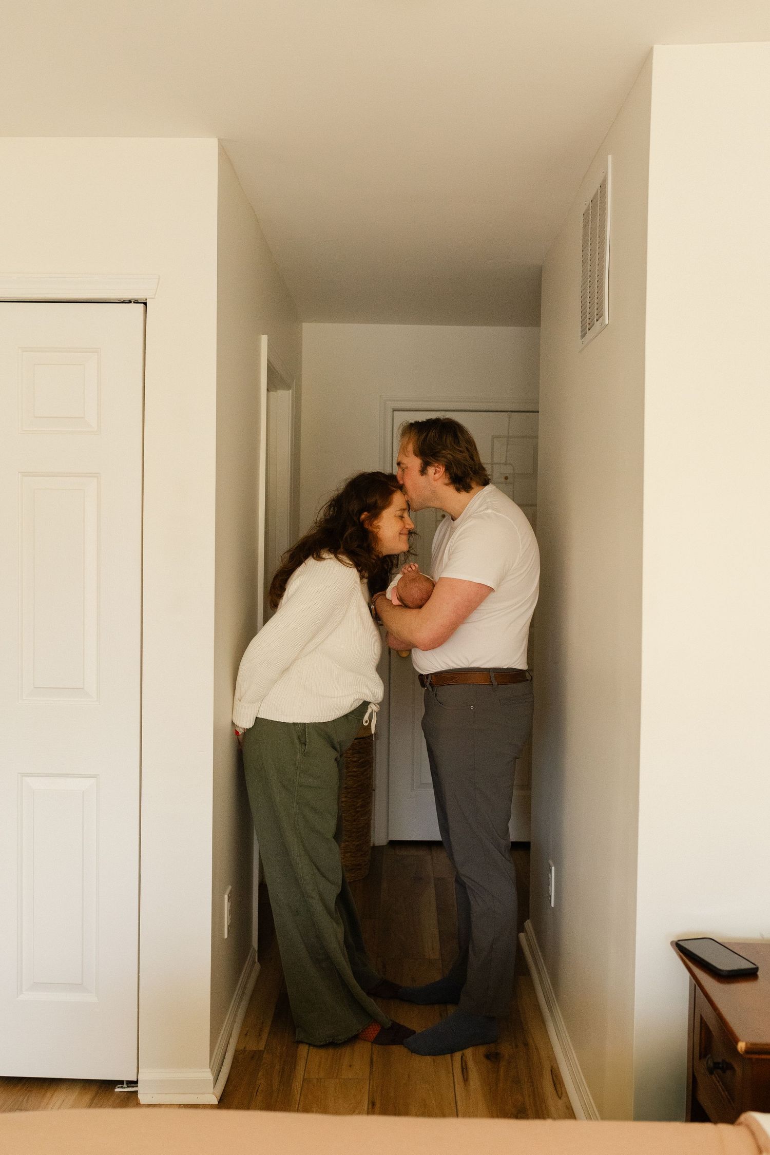 Couple sharing a tender moment together in a narrow home hallway holding their newborn.