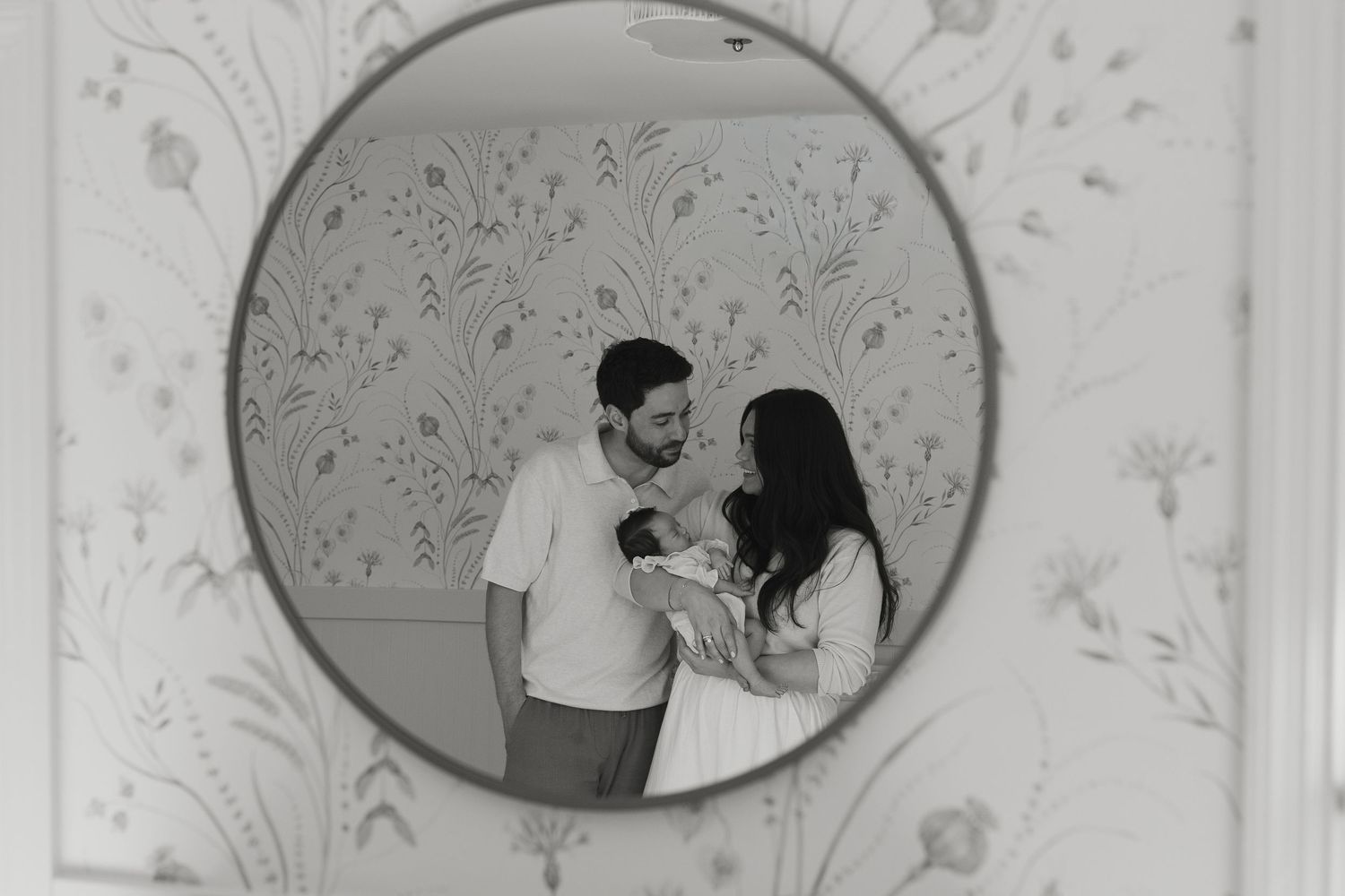 Black and white mirror reflection of new parents lovingly holding their newborn baby.