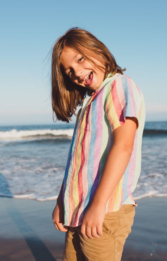 Happy child with long hair wearing a colorful striped shirt laughing at the beach during sunset.