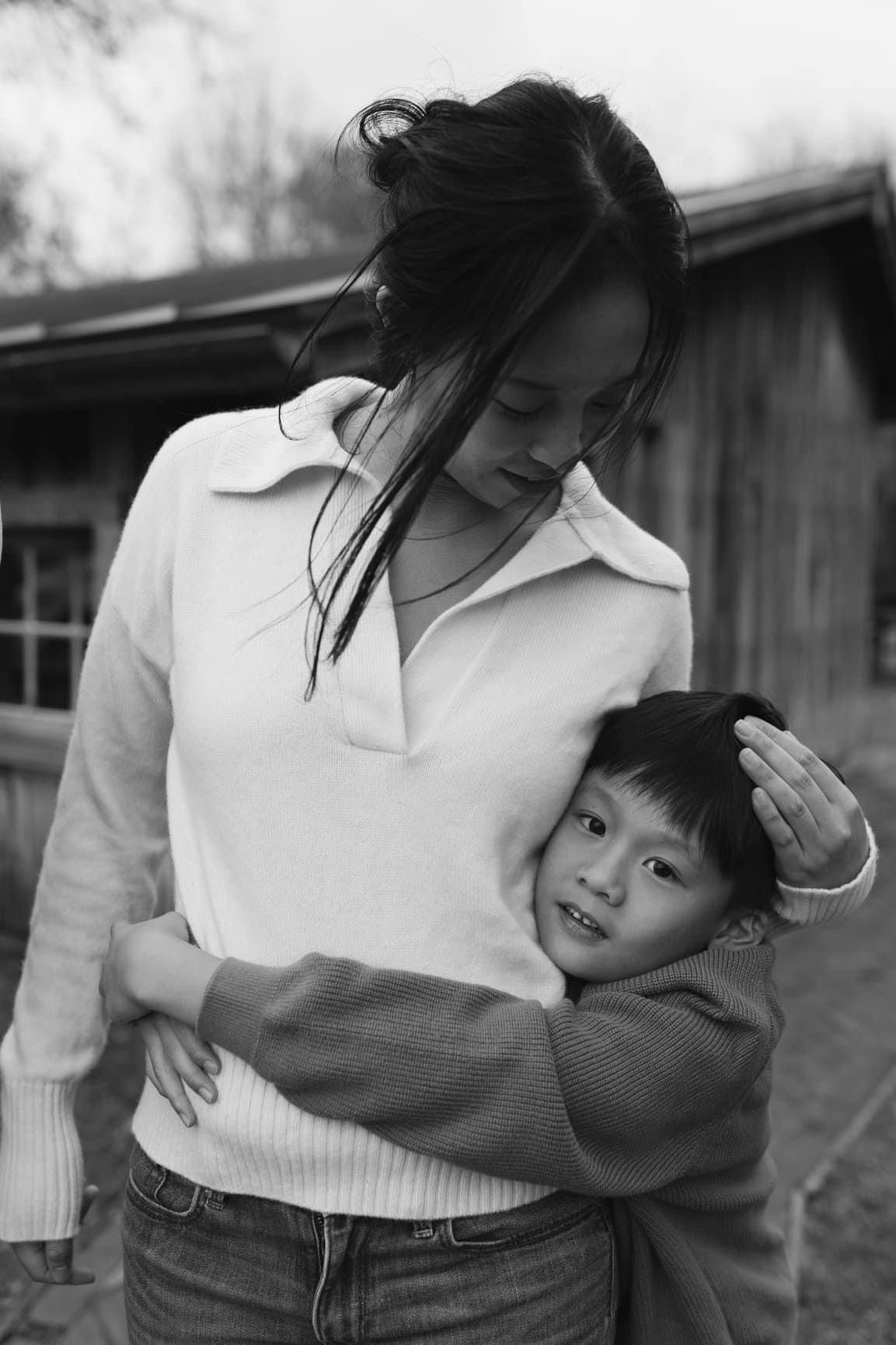 A mother tenderly embraces her young child outdoors in a black and white portrait photo.