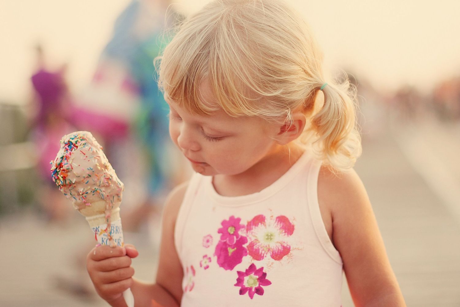 Young child in a white dress enjoying ice cream on a sunny summer day.