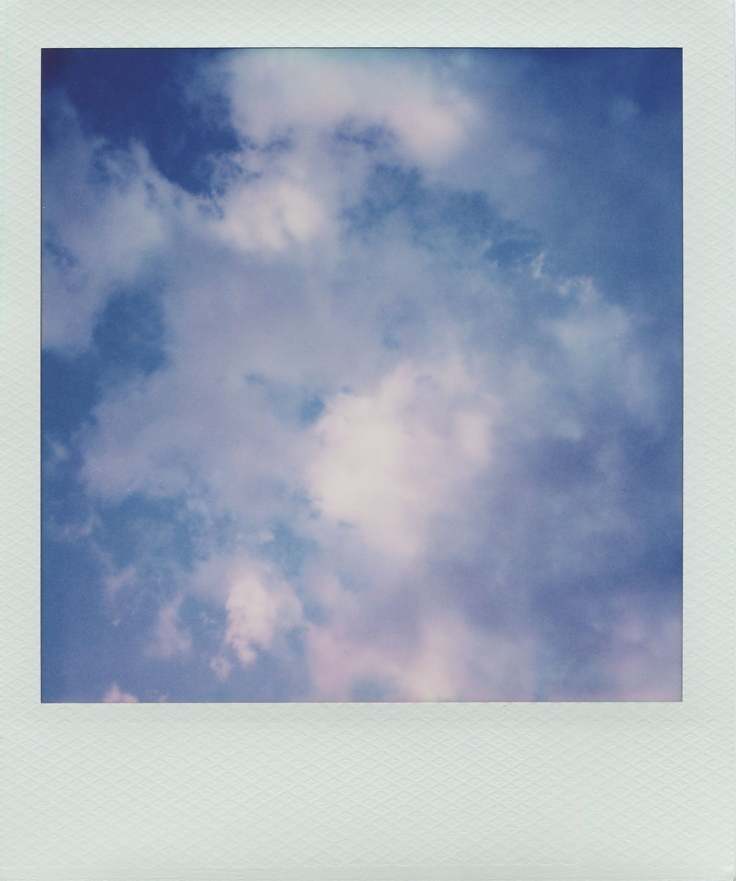 Dreamy polaroid photo of a blue sky with soft white and pink fluffy clouds on a sunny day.