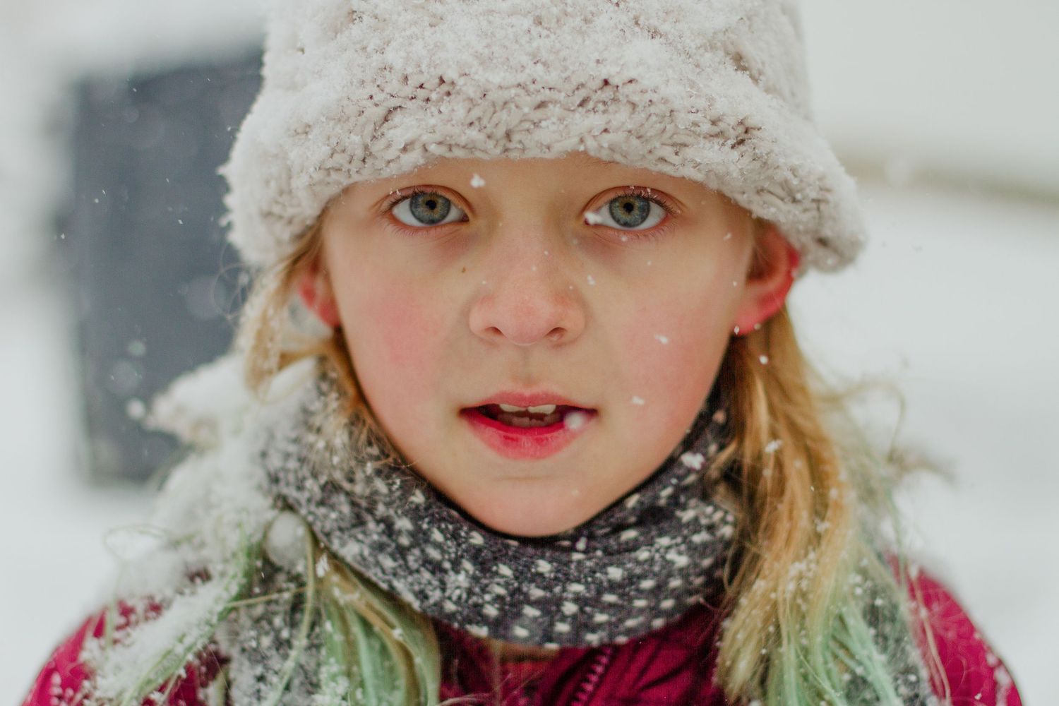 Child wearing a winter hat and scarf smiling in the snow.