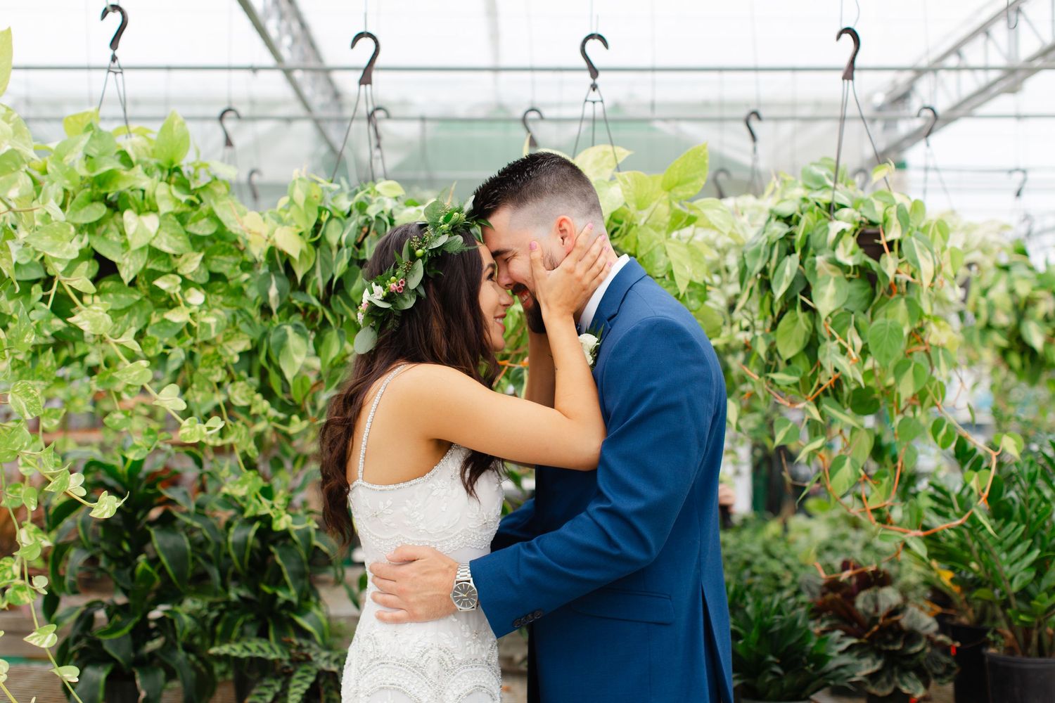 A couple shares a romantic moment in a lush greenhouse, with the bride wearing a floral crown.