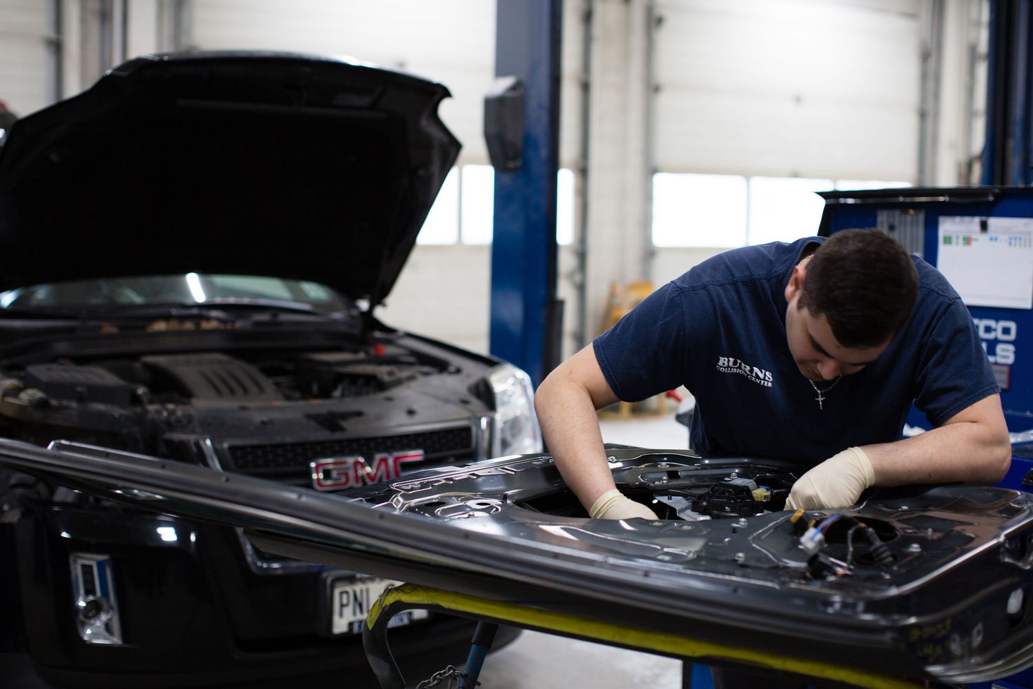 Mechanics working under the hood of multiple cars in an auto repair shop.