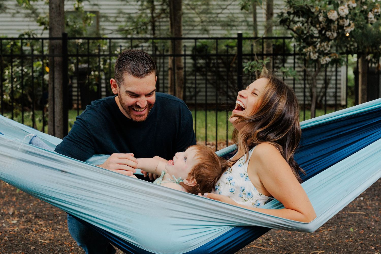 Joyful family laughing together in a blue hammock in their backyard.