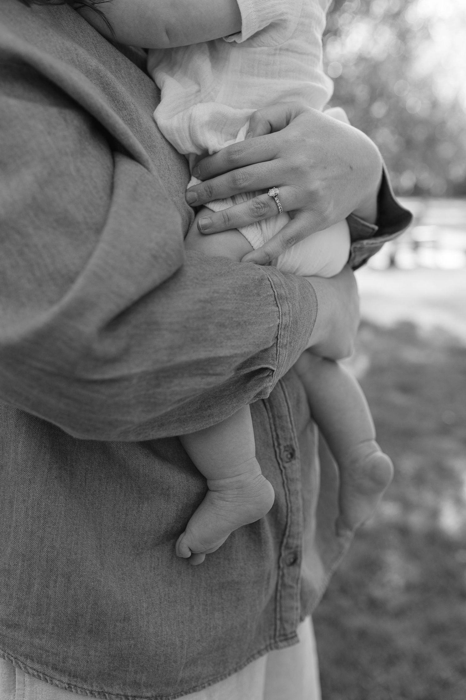 Black and white close-up of mother holding baby, showing tiny feet and ringed hand.