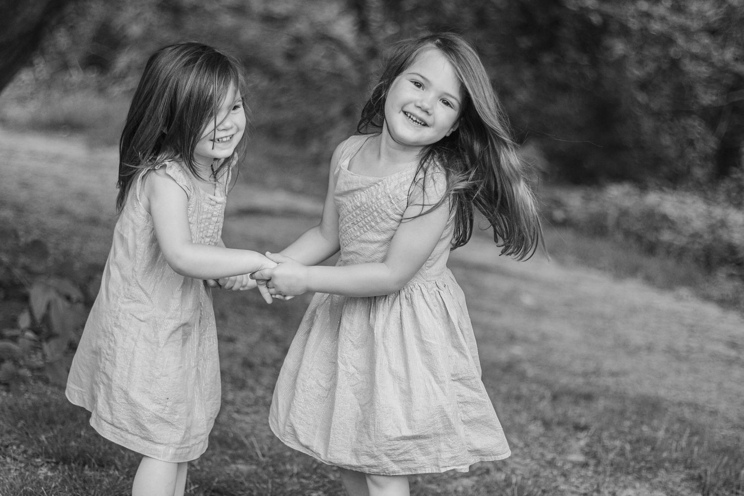 Black and white photo of two laughing girls in dresses holding hands and playing outdoors.