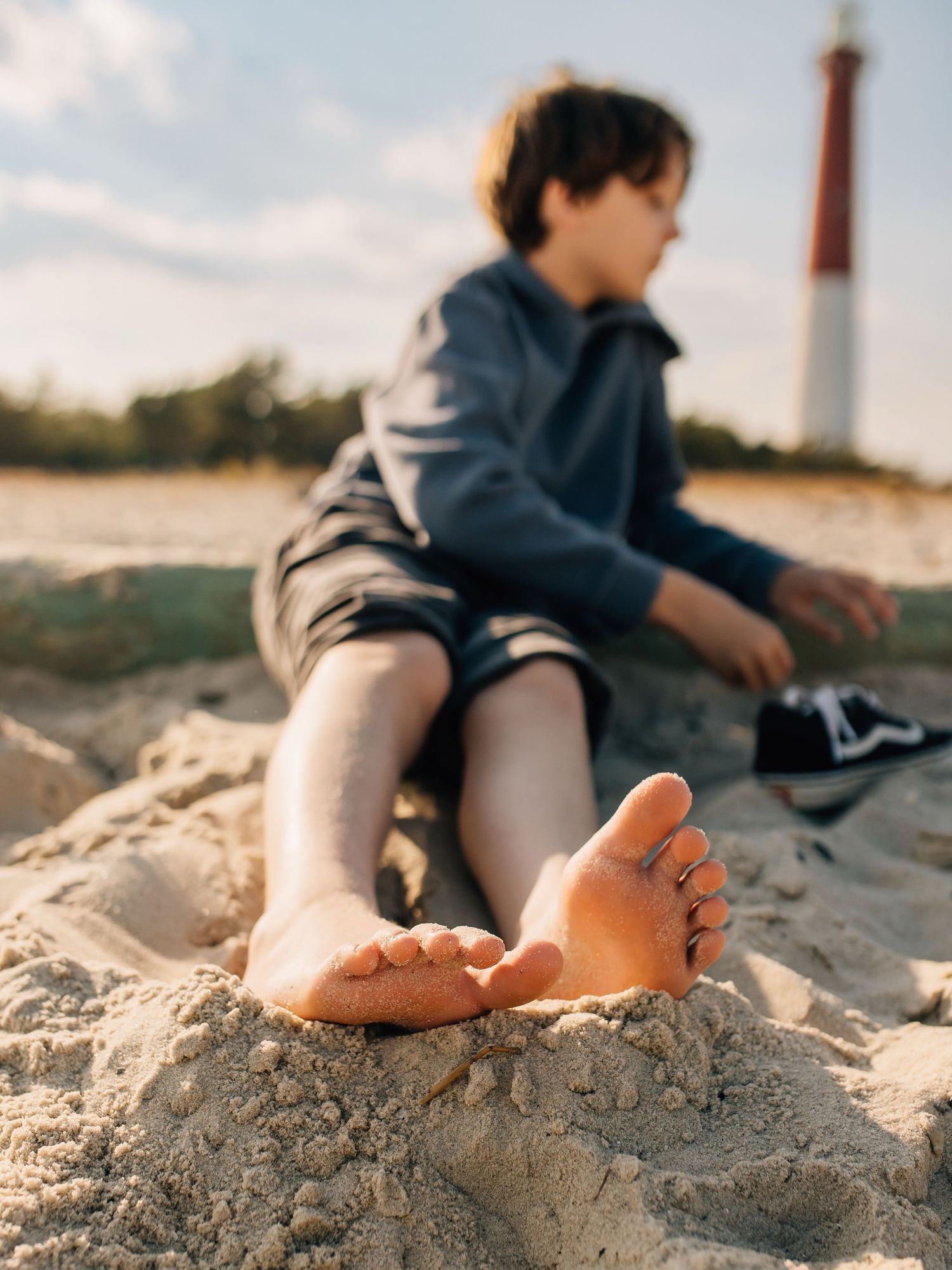 Bare feet in sand on a beach with someone sitting in the background during sunset.