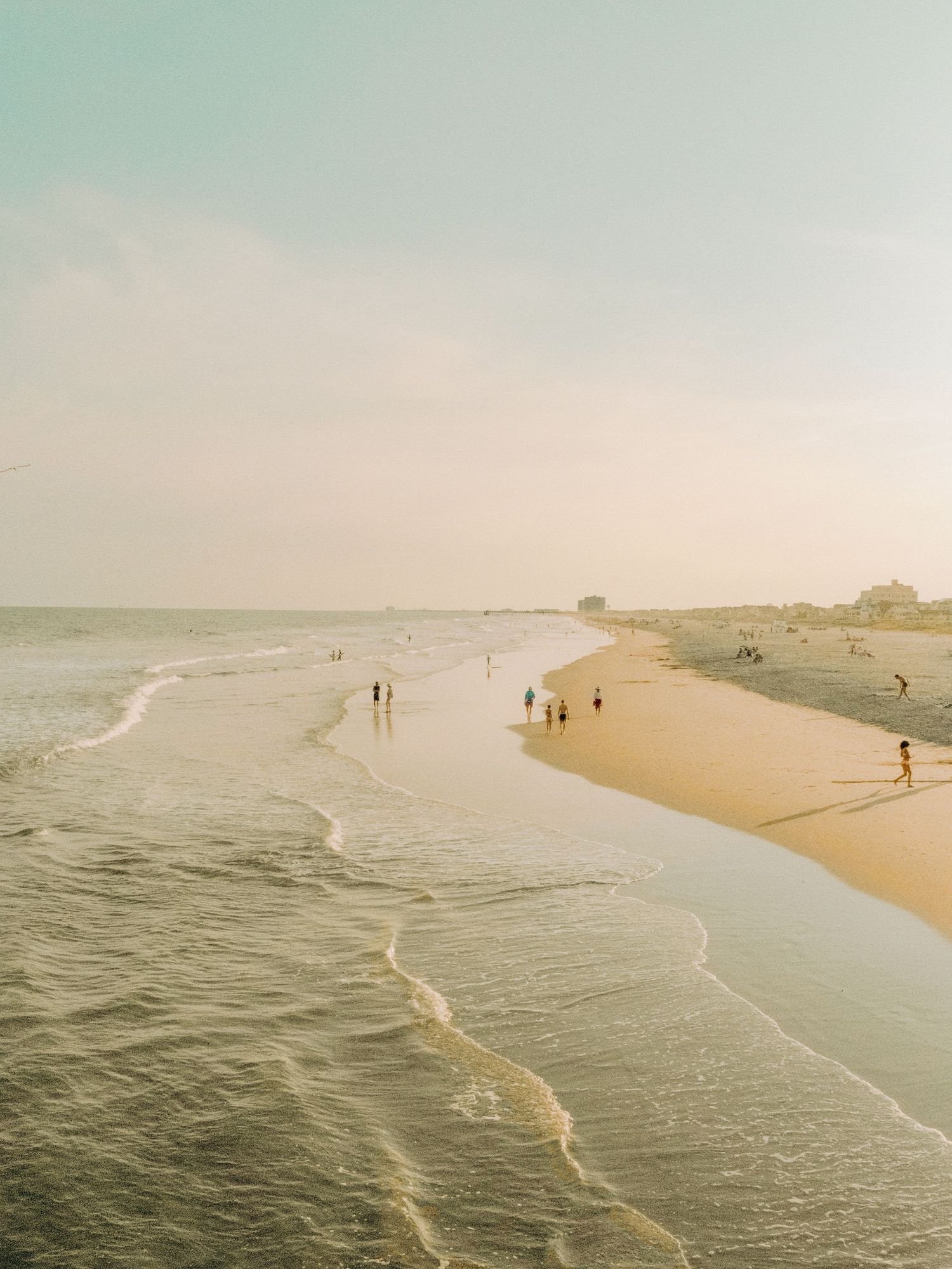 Aerial beach landscape with gentle waves rolling onto golden sand at sunset.