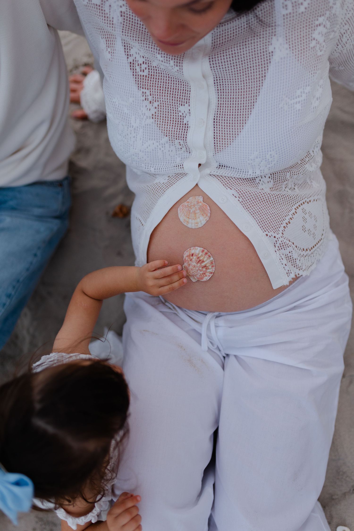 A young child touches decorative stickers on a pregnant woman's bare belly during a family maternity photoshoot.