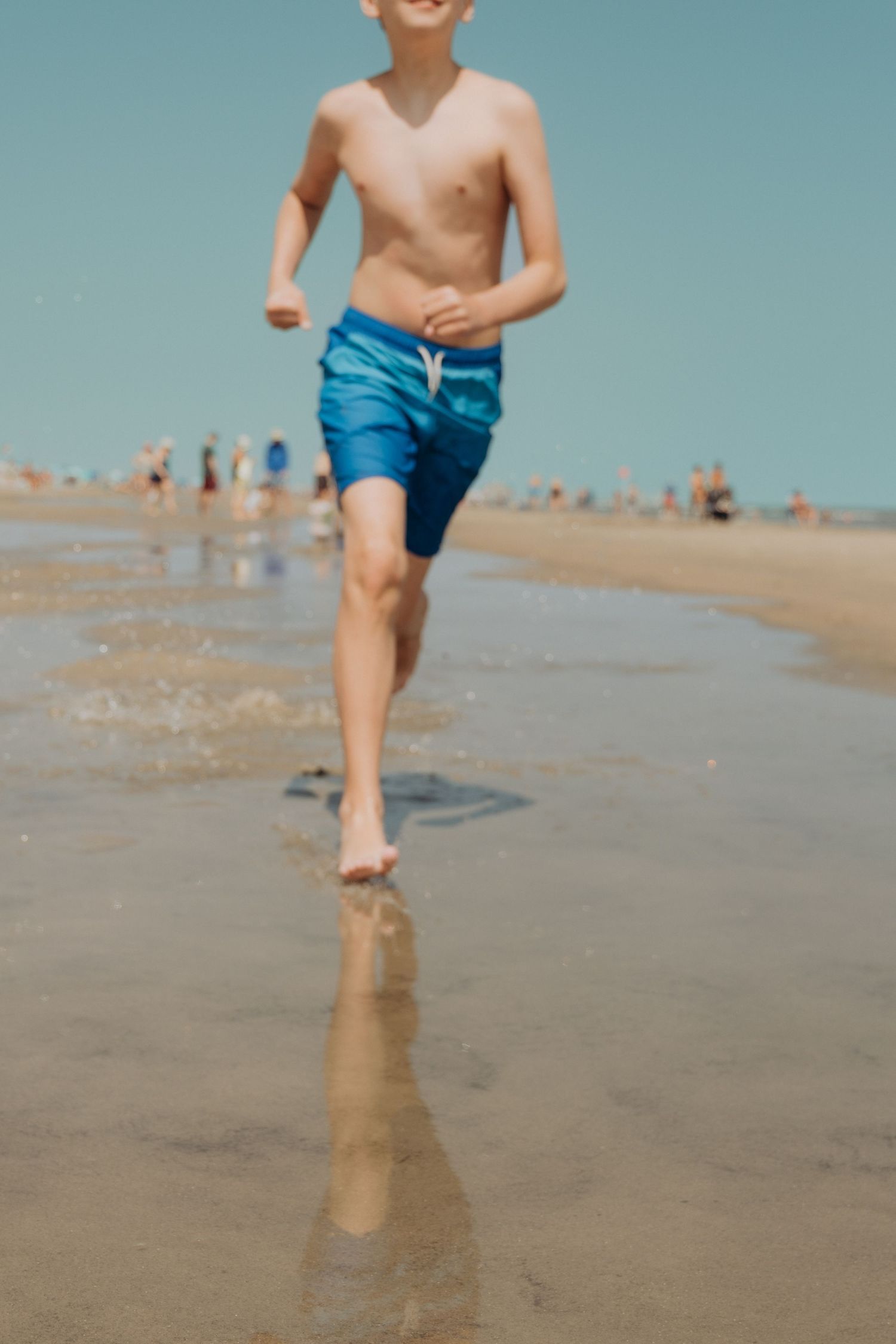 Bare feet running along wet sand on a sunny beach.