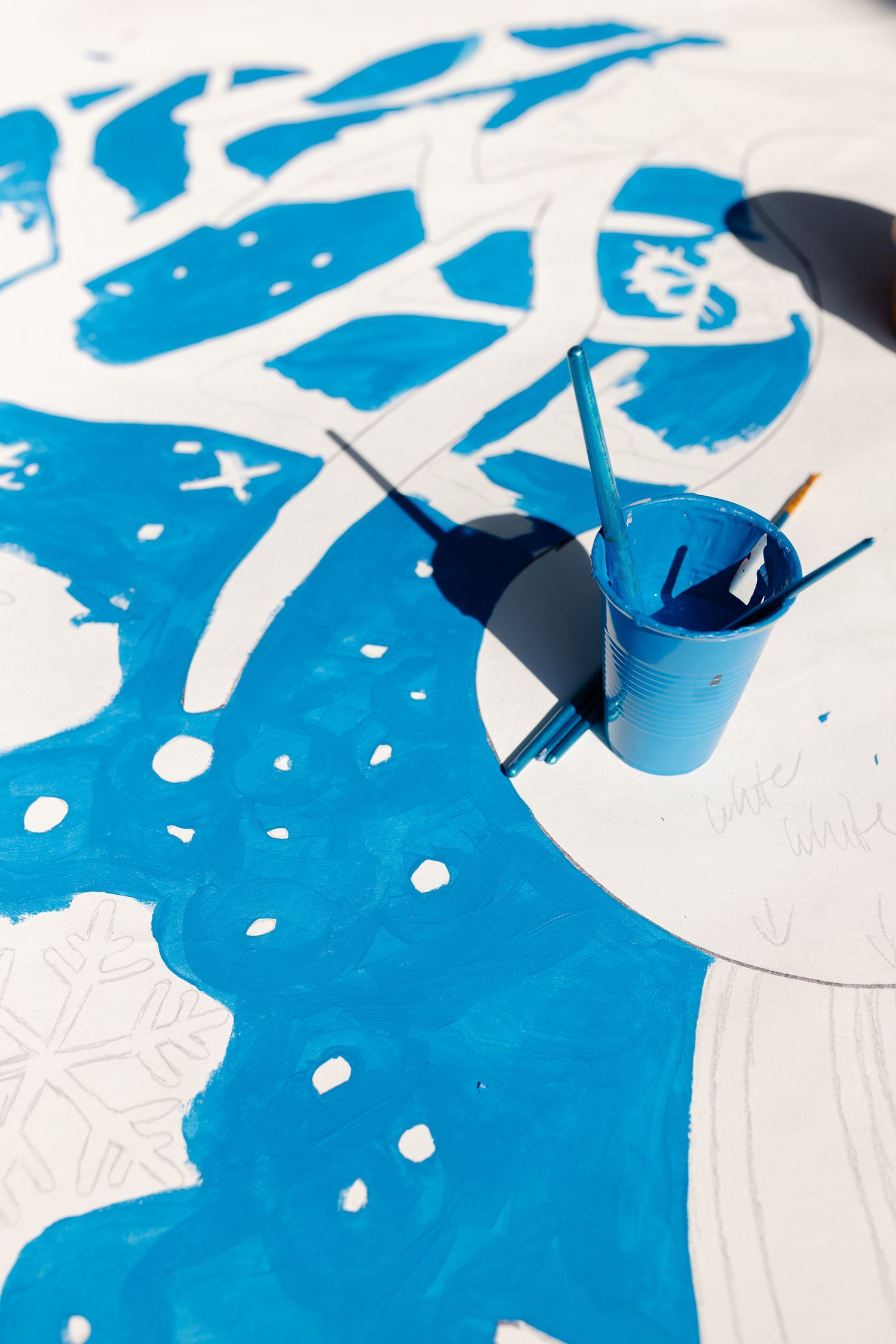 Blue and white mural painting in progress with brushes in paint cup outdoors.