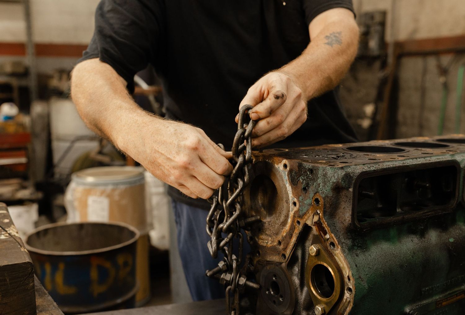 Mechanic holding a greasy chain while working on a vintage engine block in an auto repair shop.