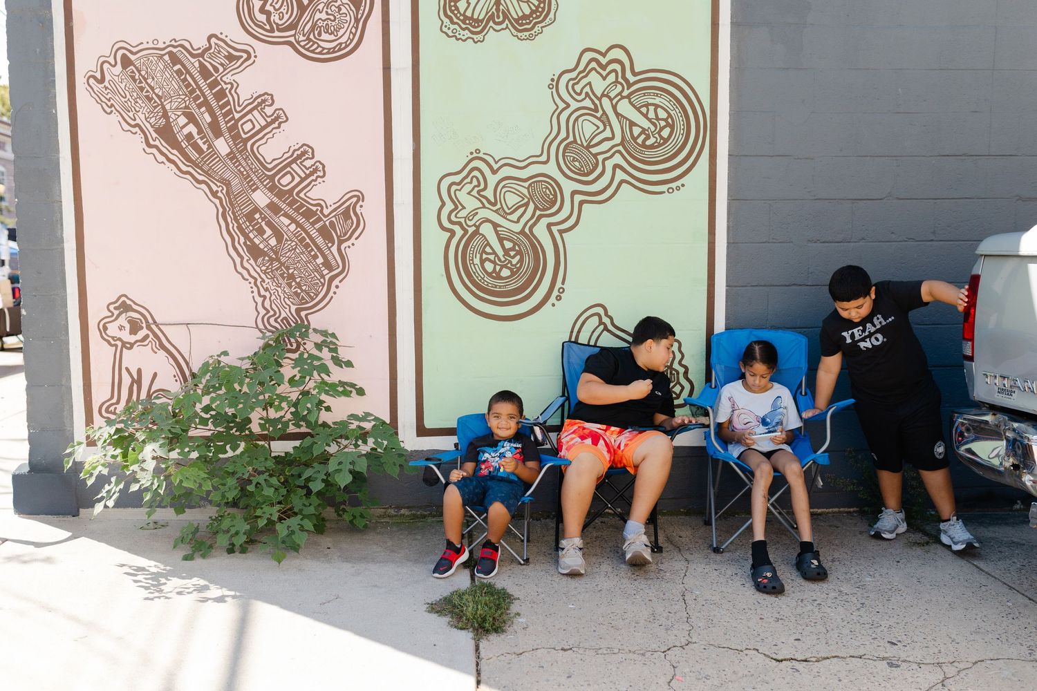 Family sitting in chairs against a colorful mural wall outdoors on a sunny day.