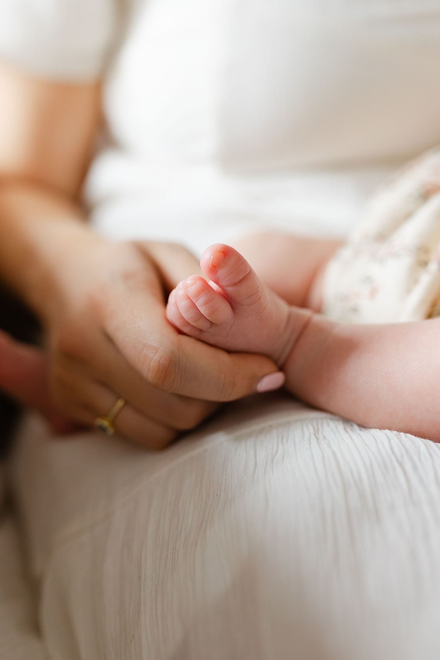 Close-up of mother gently holding newborn baby's tiny feet in her hands, wearing a gold ring.