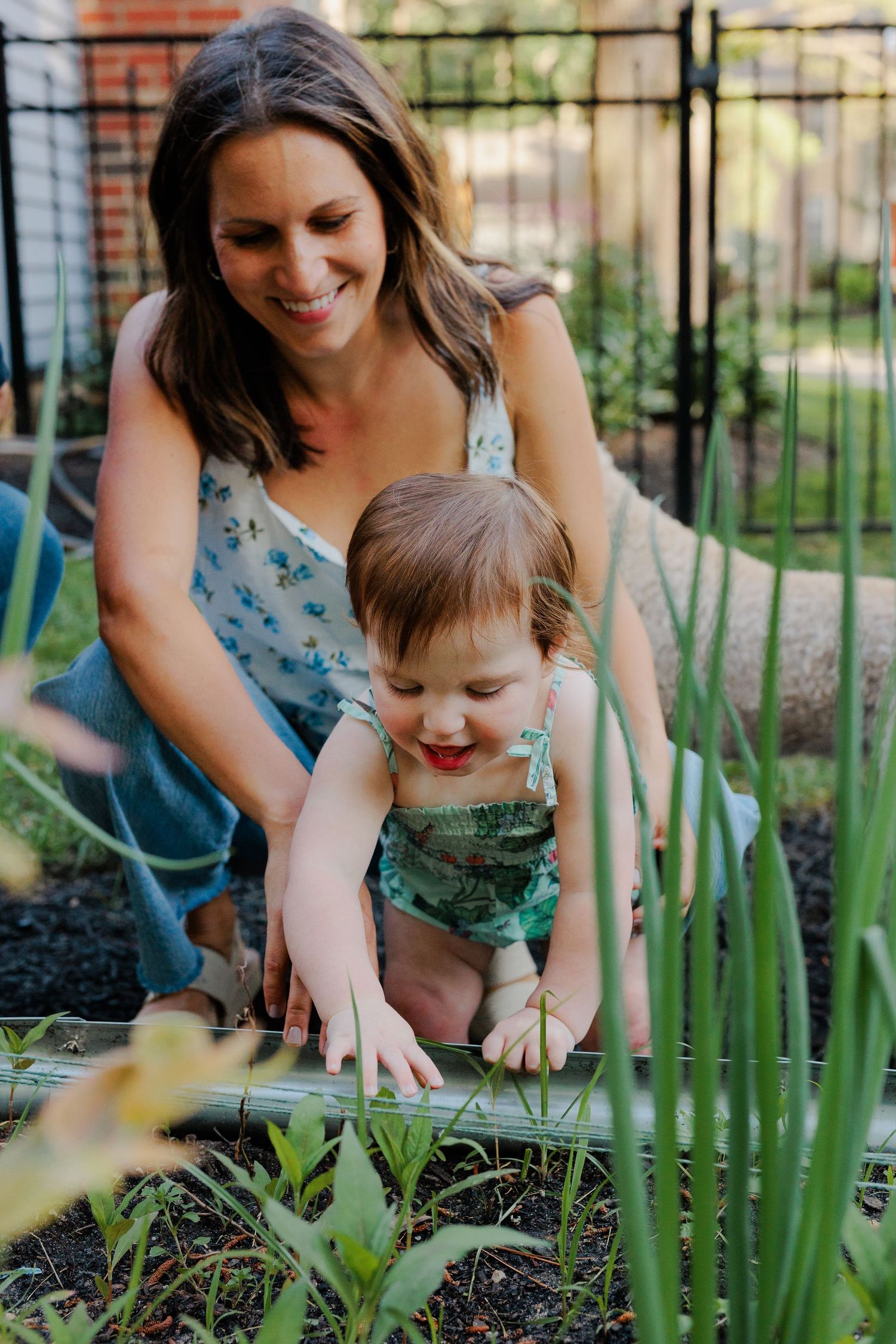 Smiling mother and baby girl exploring a vegetable garden together outdoors.
