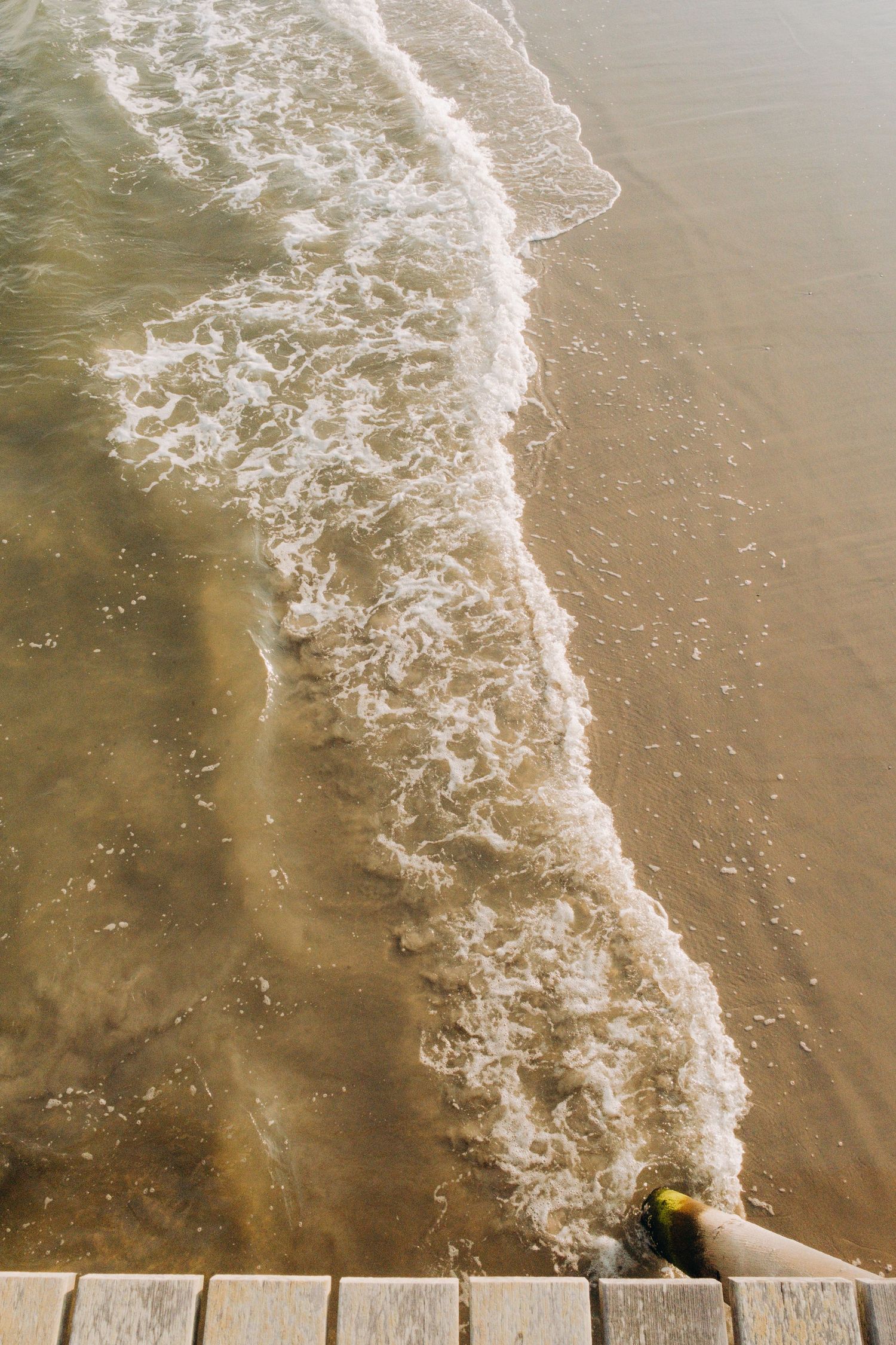Ocean waves crash against the sandy shore creating white foam patterns along the beach.