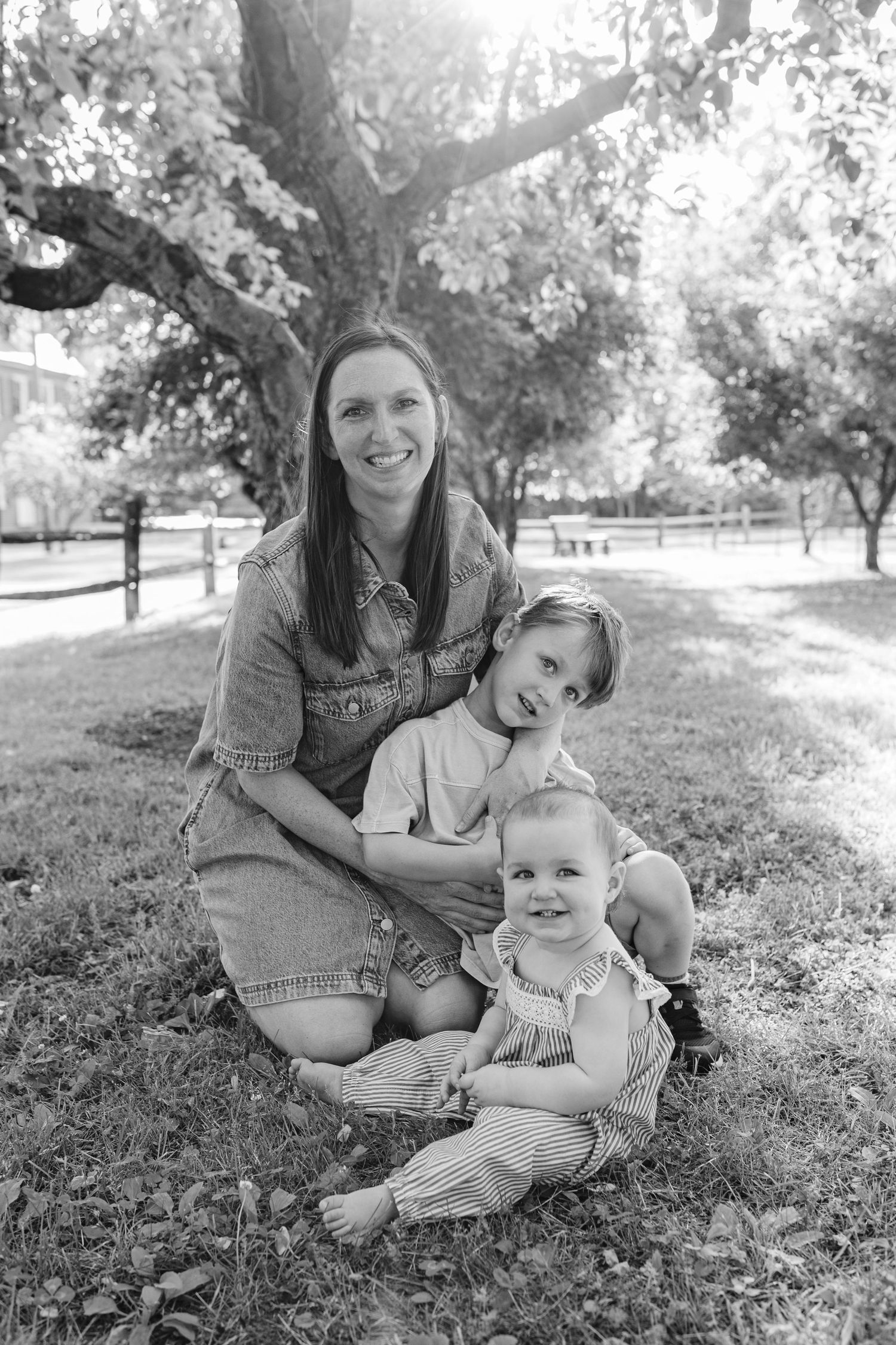Black and white portrait of smiling mother with two young children sitting under a tree.