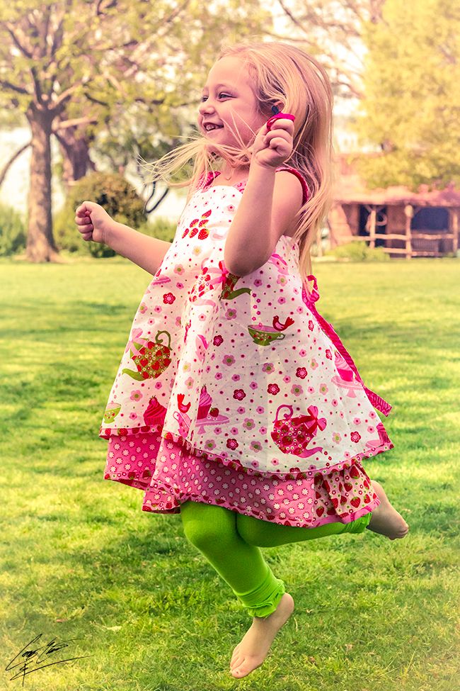 Joyful little girl in a colorful pink layered dress spinning and jumping in a green park.