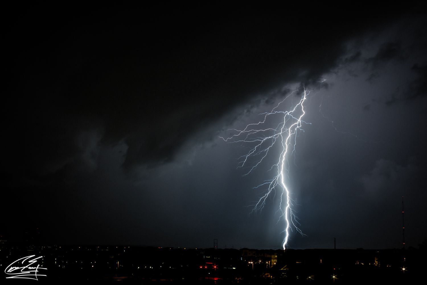 A dramatic lightning bolt strikes during a nighttime thunderstorm over a city skyline with dark storm clouds.