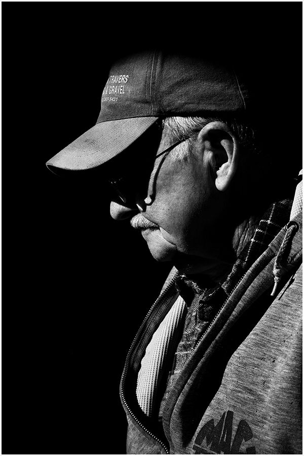 Dramatic black and white side profile of an elderly man wearing a cap and glasses.