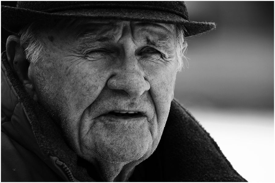 Dramatic black and white close-up portrait of an elderly man wearing a hat with weathered features.