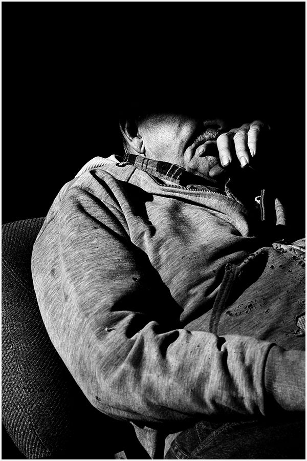 Black and white photo of a person resting their head on their hand while seated on a couch.
