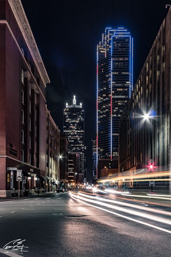 Long exposure night photography of Dallas city street with light trails and illuminated skyscrapers.