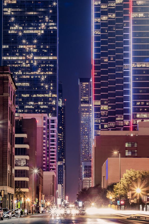 Vibrant night cityscape with illuminated skyscrapers and light trails on urban street.