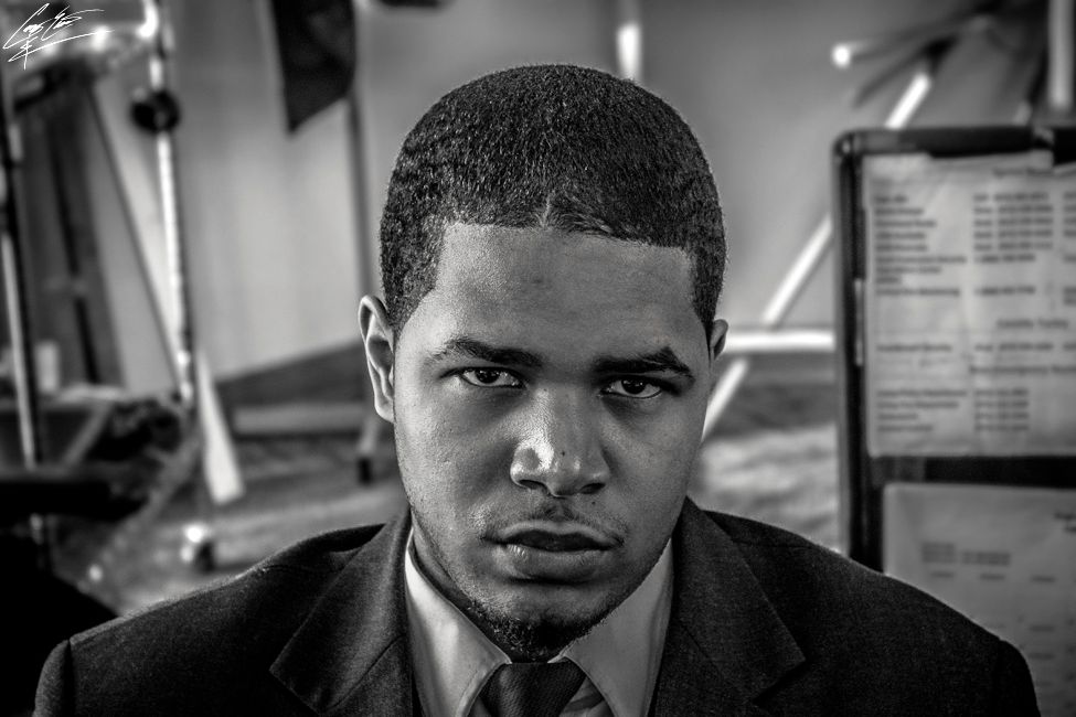 A black and white portrait of a man in a suit staring directly at the camera with a serious expression in an office setting.