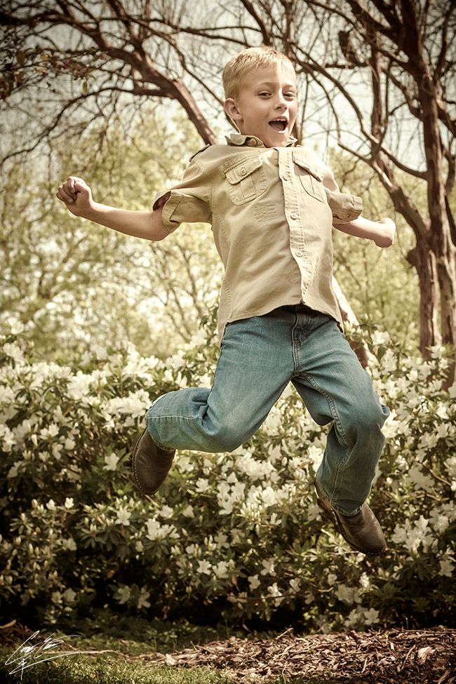 A young child mid-jump outdoors, surrounded by trees and sunlight, capturing a sense of motion and joy.