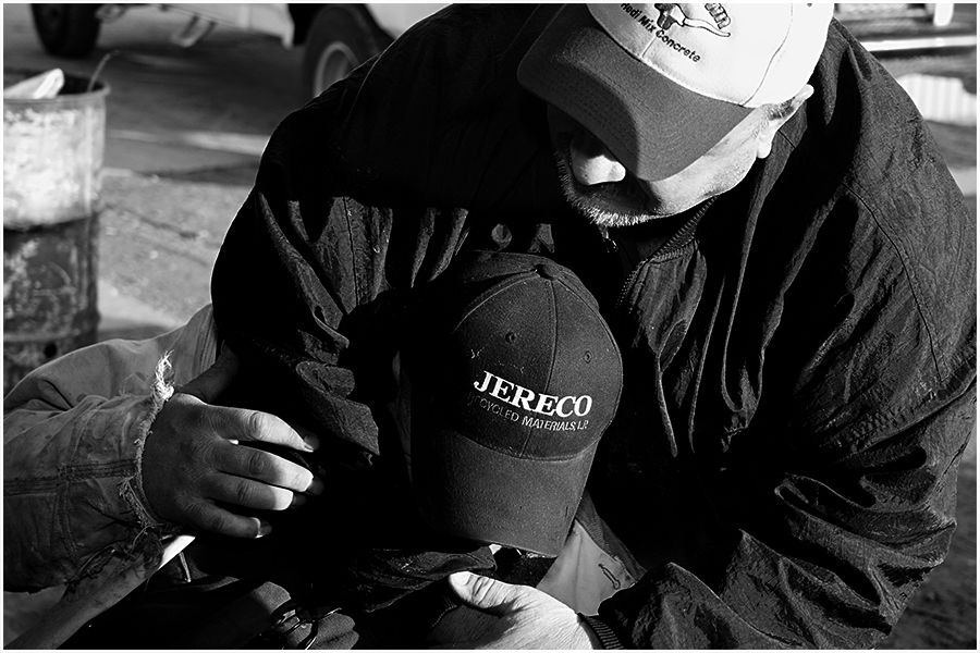 Black and white image of a man holding a Jereco branded baseball cap outdoors.
