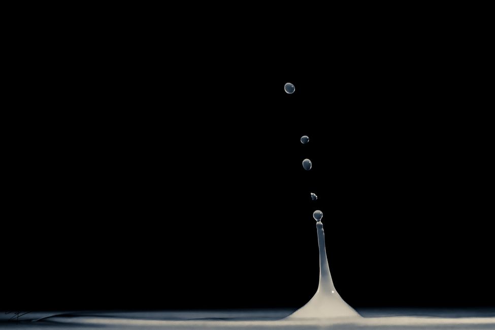 Minimalist black background macro photo of water droplets rising above a liquid surface column.