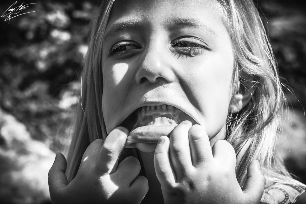 A black and white portrait of a girl stretching her mouth wide with her fingers, creating an exaggerated expression.