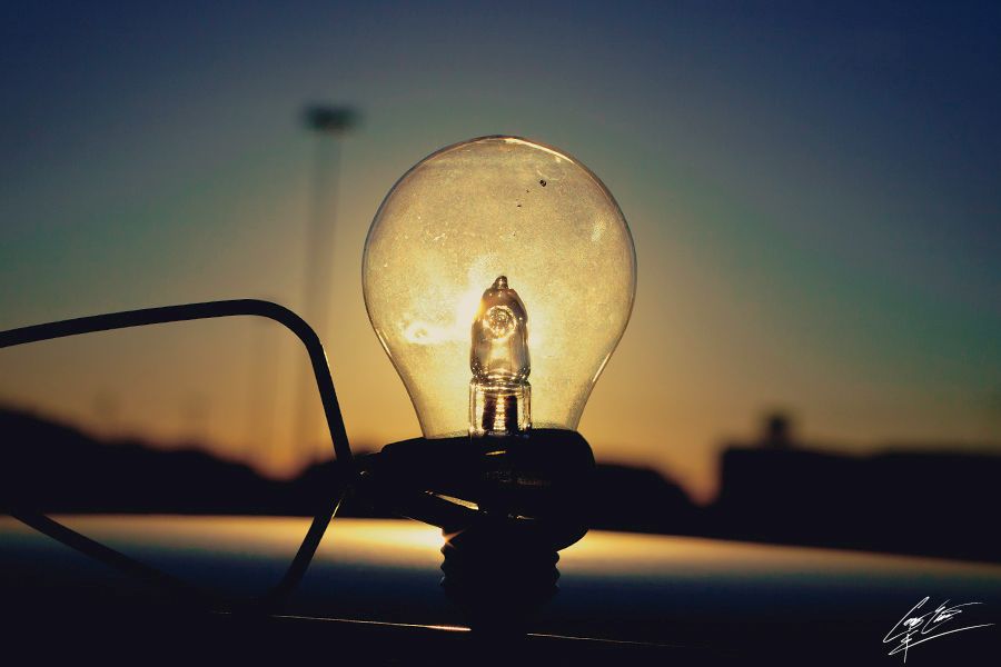 A glowing incandescent light bulb photographed against a warm sunset sky at dusk.