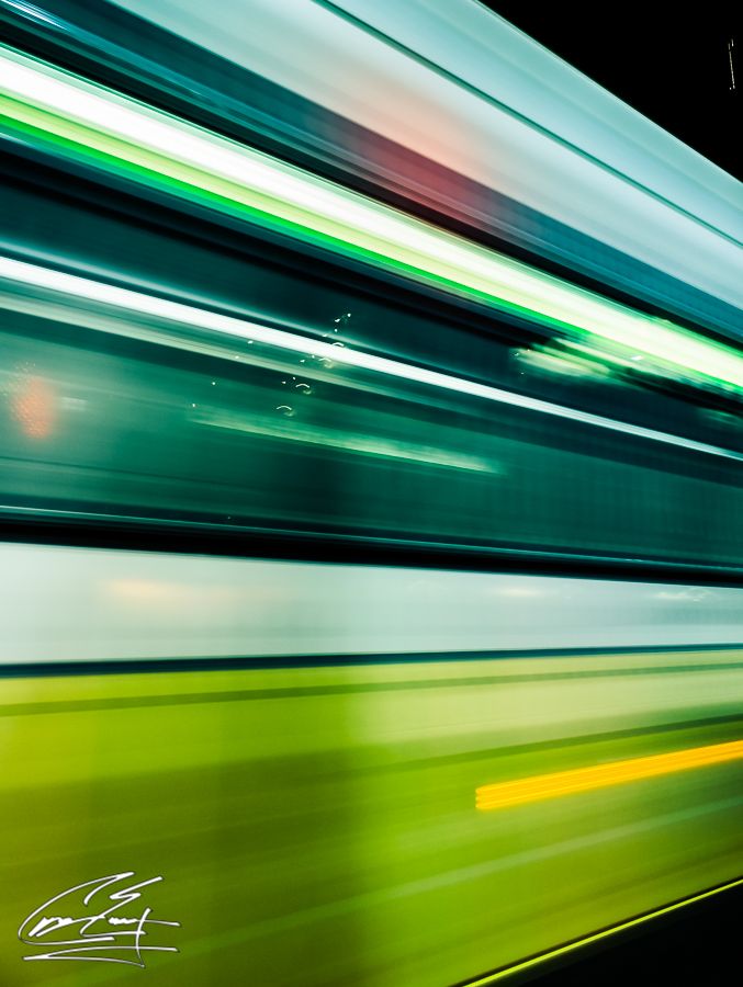 Long exposure shot of a green and white subway train creating colorful motion blur streaks.