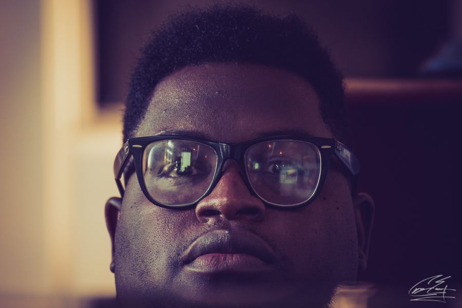 Close-up portrait of young man wearing large glasses with light reflections in warm tones.