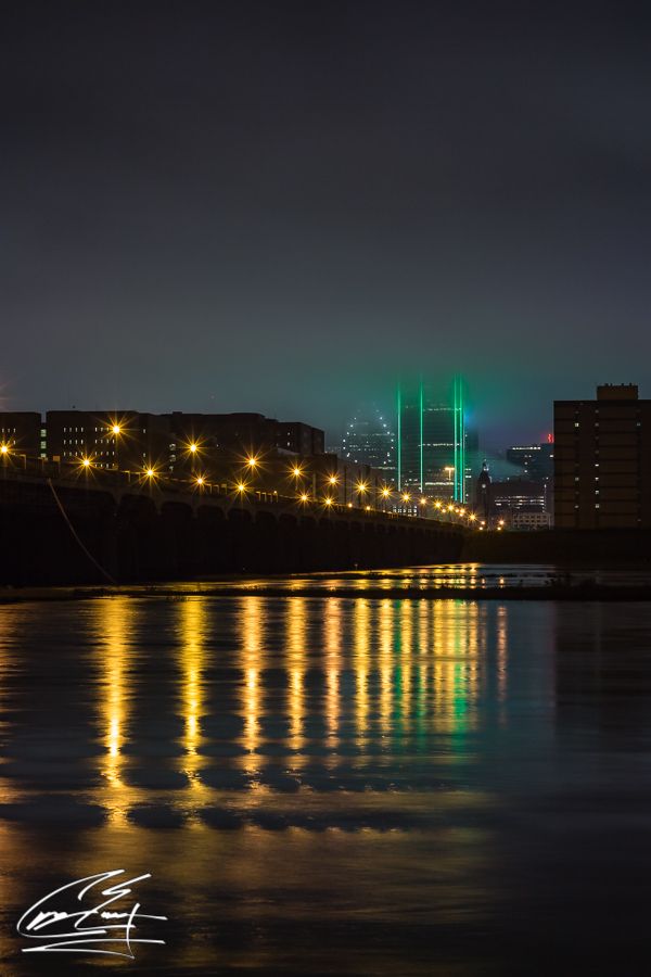 Night cityscape reflection of Dallas skyline lights shimmering on calm river water under dark sky.