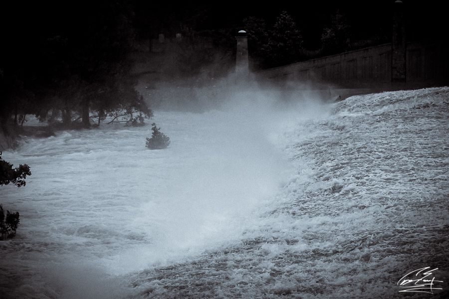 Powerful white water rapids crashing near a lighthouse during a storm or flood event.
