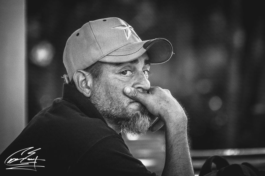 Thoughtful middle-aged man wearing baseball cap resting chin on hand in black and white portrait.