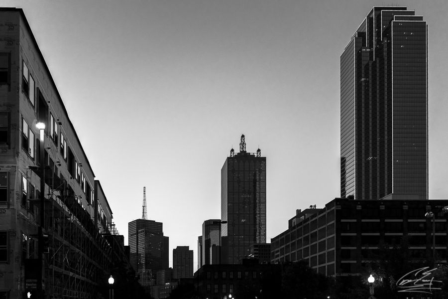 Black and white cityscape of downtown skyscrapers silhouetted against a clear sky at dusk.