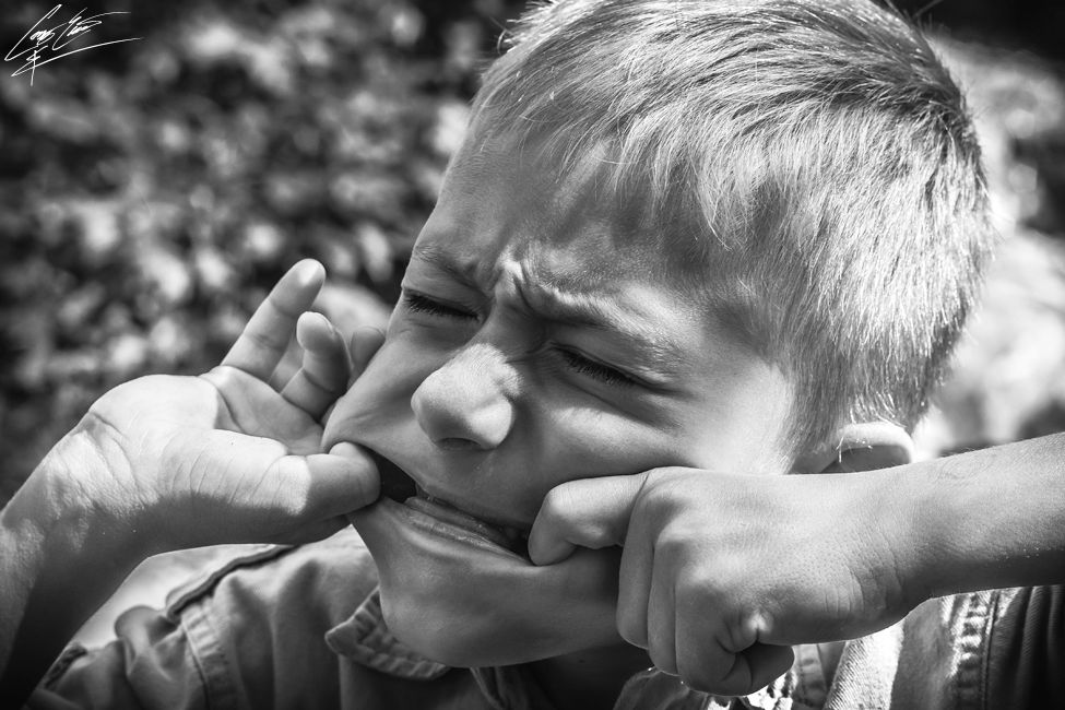 A black and white portrait of a young boy with his face pulled outward, creating a distorted expression.