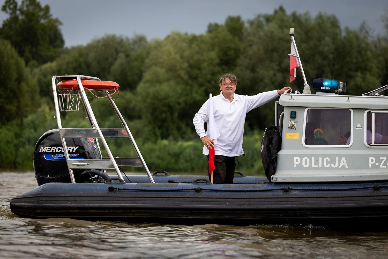 Man in white chef coat standing on police patrol boat on river.