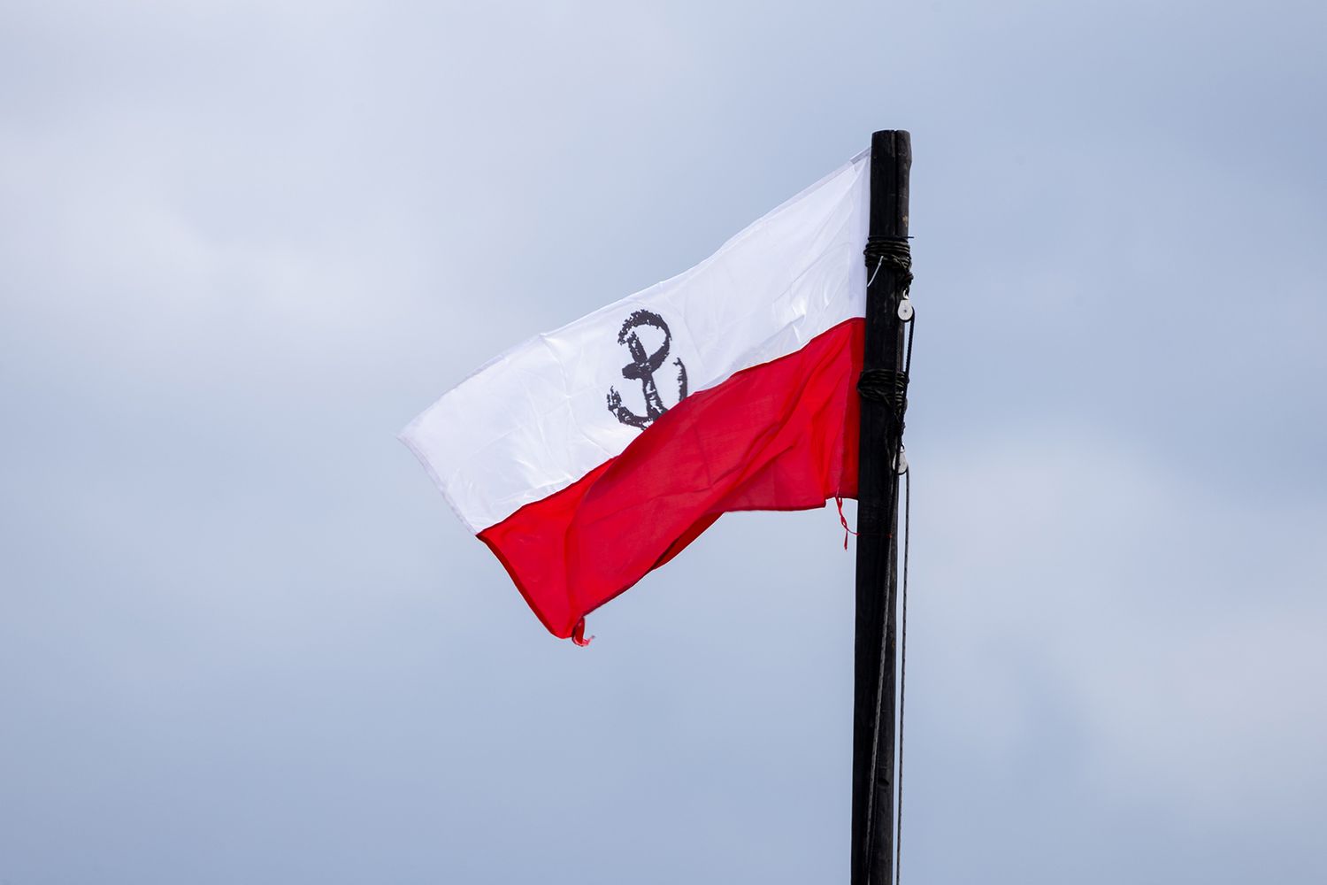 Polish naval ensign flag with anchor symbol waving in cloudy sky.