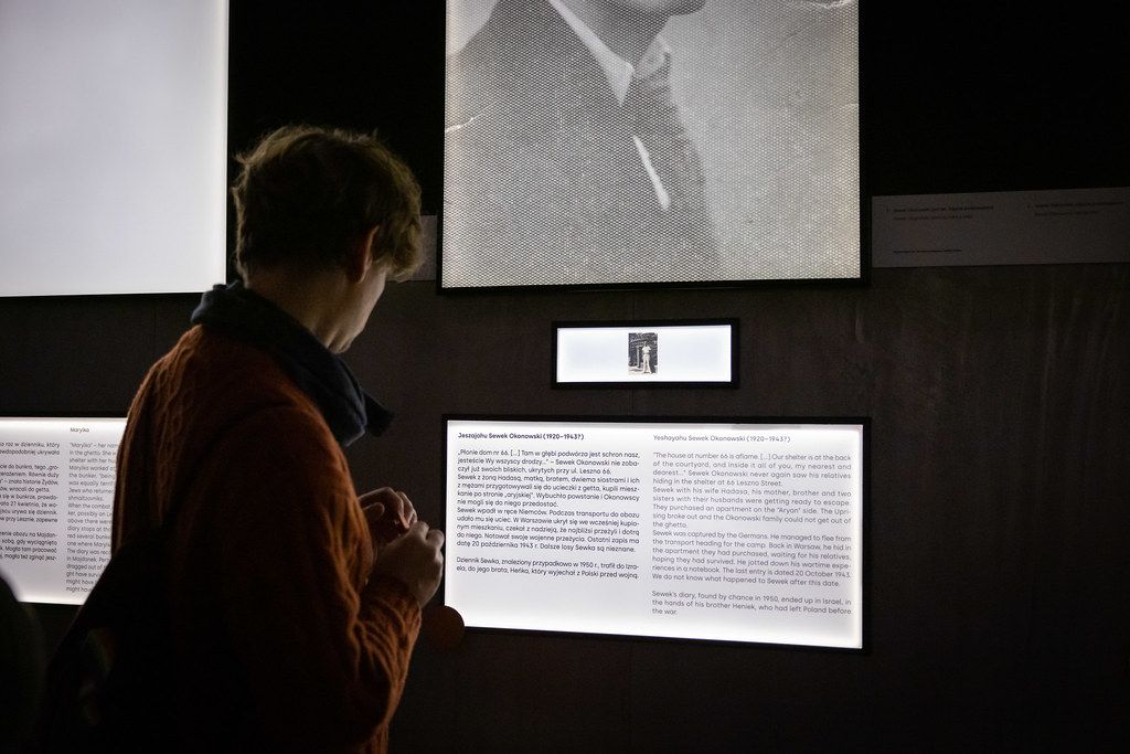 Visitor reading illuminated text panels in a dark historical museum exhibition.
