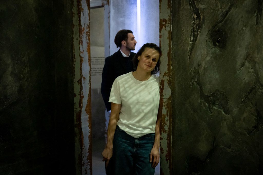 Two people standing in a narrow deteriorated corridor during a theatrical performance.