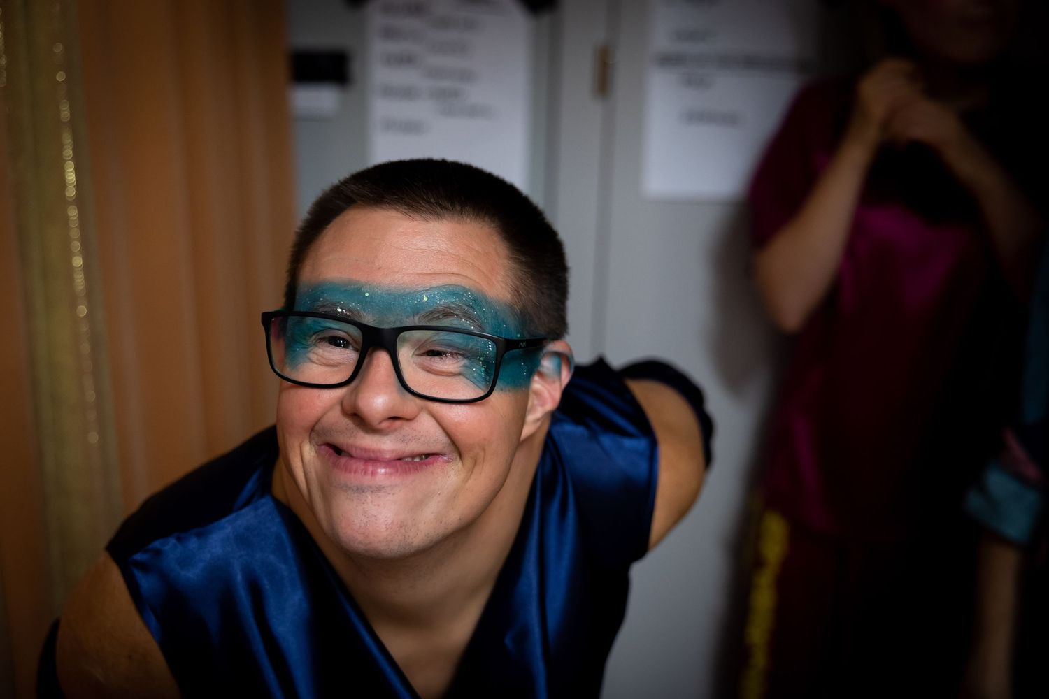 Smiling person wearing glittery blue glasses and a blue cape at a costume event.
